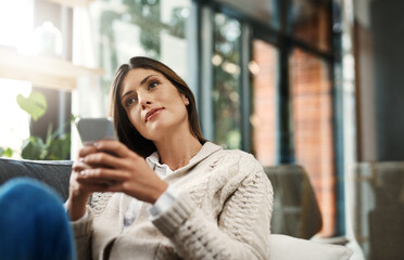 Maybe its time I sent that message. Shot of an attractive young woman looking thoughtful and sending text messages while relaxing on her sofa at home.