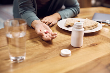 Close up of woman taking pills during breakfast at dining table.
