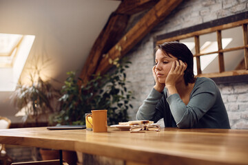 Pensive woman has no will to eat because she is feeling depressed at home.