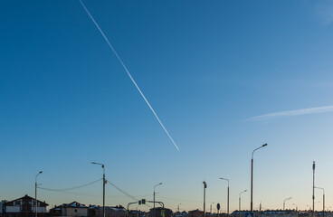 A flying plane over the city leaves a white trail
