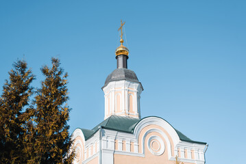 Fototapeta na wymiar Faith and religion concept. Christian church with golden dome and cross against clear blue sky. Exterior of an ancient religious building outdoors