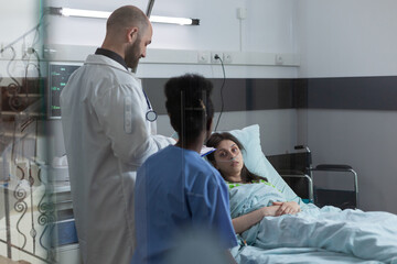 Fototapeta premium Medical doctor and nurse doing consult in private ward to recovering woman in hospital bed after surgical intervention. Patient with nasal cannula looking at health care professionals.