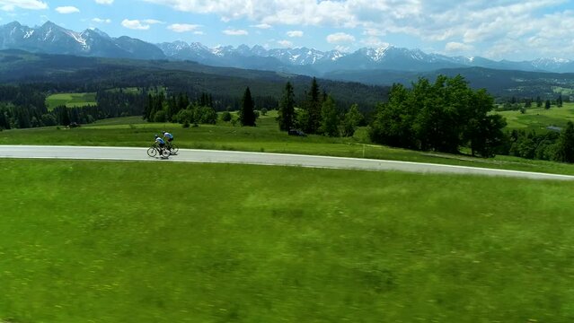 Aerial view of mountain empty road and two bikers cycling. In the background wide mountain range and epic alpine view. Concept: Vacations in the mountains, traveling on a bike