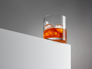 Glass of elegant whiskey with ice at the edge of a wooden cube.