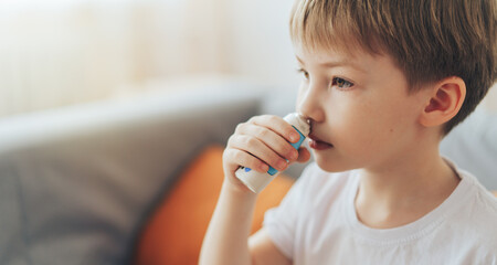 Little boy uses nasal spray while sitting on the couch.