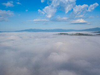 Naklejka na ściany i meble Flight over fog in Ukrainian Carpathians in summer. Mountains on the horizon. A thick layer of fog covers the mountains with a continuous carpet. Aerial drone view.