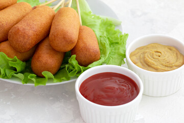 american fast food. corn dog with fresh lettuce, ketchup and mustard on a light background