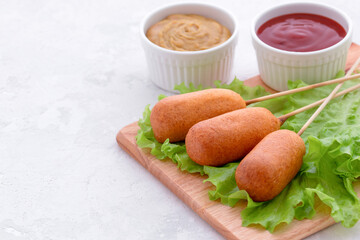 american fast food. corn dog with fresh lettuce, ketchup and mustard on a light background