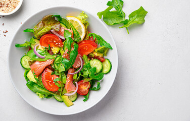 Salmon salad with green leaves, avocado and tomatoes on a gray background.