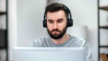 Confident handsome bearded man wearing wireless headphones use laptop modern workplace - Powered by Adobe