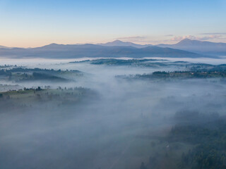 Fototapeta premium Flight over fog in Ukrainian Carpathians in summer. Mountains on the horizon. Aerial drone view.