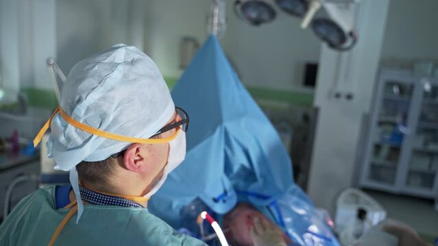 Adult surgeon moving the device tool input into patient. High angle view. Surgery room at backdrop in blur.