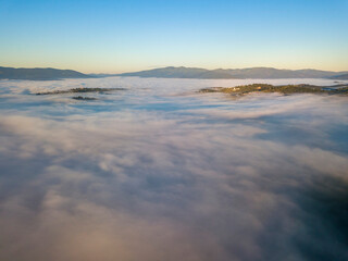 Flight over fog in Ukrainian Carpathians in summer. Mountains on the horizon. A thick layer of fog covers the mountains with a continuous carpet. Aerial drone view.