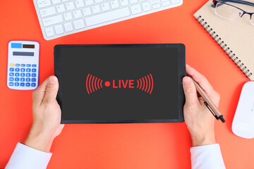 Hand uses a tablet to watch live streaming and use a video player app on the tablet's screen. On a red background