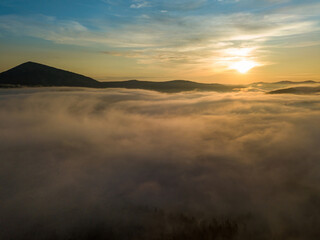 The rays of dawn over the fog in the Ukrainian Carpathians. Aerial drone view.