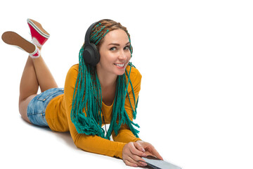 Young Winsome Positive Caucasian Female with African American Dreadlocks Listens Music in Wirreless Headphones Smartphone While Laying on Floor Over White.