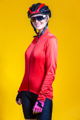 Winsome Female Road Cyclist in Professional Warm Outfit Standing In Red Autumn Jacket and Goggles With Reflections Against Yellow Background.