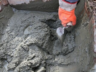 hand working with a thick gray cement mortar at a construction site, a hand in a rubber glove picks up a concrete slurry from an iron container using a trowel