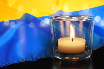 Burning candle and Ukrainian national flag on black table, closeup view