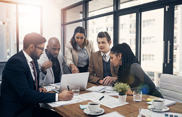 Fototapeta premium Teamwork is the ultimate productivity booster. Shot of a group of young businesspeople using a laptop together during a meeting in a modern office.