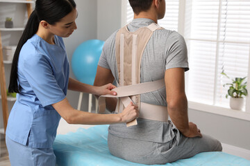 Orthopedist helping patient to put on posture corrector in clinic. Scoliosis treatment