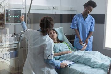 Nurse putting pulse oximeter on patient finger while doctor setting up central line catether with...