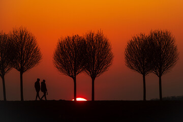 two figures walk along a path straight towards the rest of the setting sun