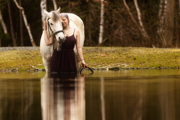Youngwoman with white hair standing in the water with a white horse