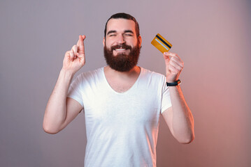 Portrait of a wishing bearded man crossing fingers while holding a card.