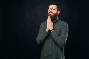 Serious bearded man is holding hands and eyes closed for prayer.