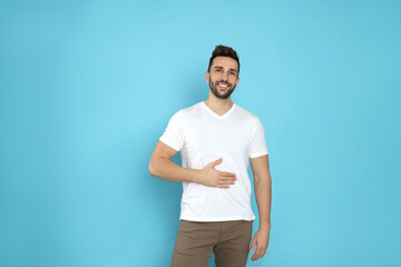 Happy man touching his belly on light blue background. Concept of healthy stomach