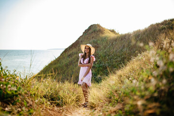 the girl runs across the field. Happy girl. Long hair. White dress. A hat with a brim. Bouquet of daisies. A young girl in nature.