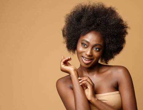 Happy African Beauty Model with Afro Hairstyle. Cheerful smiling Woman with Dark Skin and Black Coily Hair over Beige. Face and Body Care