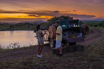 couple men and women watching the sunset during safari game drive in South Africa, sunset by a water pond lake in the Savannah of South Africa Kwazulu Natal. beautiful 