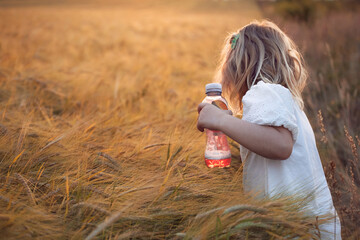 Little girl drinking refreshing fruit ice tea drink outdoors in summer. Country crop fields, golden hour sunset
