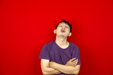 Studio portrait of an Asian young man feeling lazy and sleepy. red background.