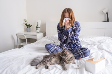 A young woman sneezes from allergies to her cat. The concept of seasonal illness and asthma. - obrazy, fototapety, plakaty