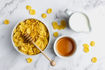 Corn flakes in white bowl with honey and milk.