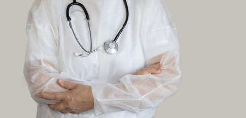 elder woman, doctor, in white medical robe, with hands one over another. nurse, medical assistant is wearing a black stethoscope on neck. medical disposable clothing. virus, other diseses protection