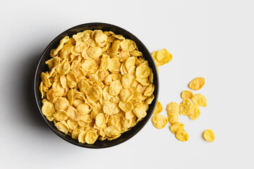 Corn flakes in dark bowl on white background.