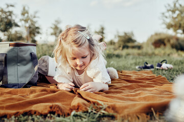 Toddler girl having fun at picnic: she is lying on picnic blanket playing with bugs and smiling