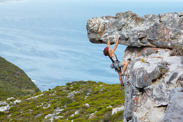Maintaining a strong grip. A young woman rock climbing up the side of a mountain.