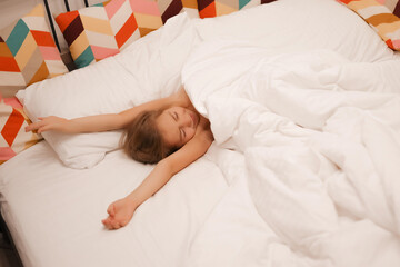 A European girl has woken up and is lying in bed with white pastel linen. The child has woken up, is pulling himself up and doing exercises