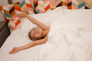 A European girl has woken up and is lying in bed with white pastel linen. The child has woken up,...