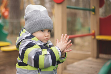 Happy little boy playing on kids playground. Outdoor activity. Portrait of joyful child in green jacket having fun outdoors. Carefree childhood.