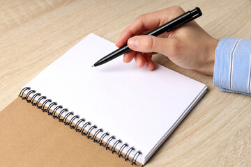 Female hand writes in blank notebook on wooden table