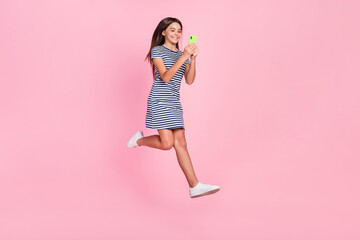 Photo of shiny sweet girl wear striped dress jumping high typing modern device isolated pink color background