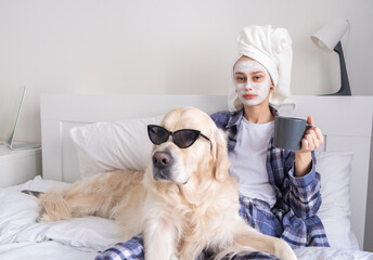 A beautiful girl does spa treatments and has fun with her dog on the bed in the morning. Young...