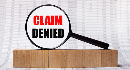 Against the background of reports on wooden cubes - a magnifying glass with the text CLAIM DENIED. Business concept