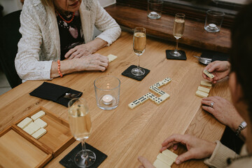 Top view of senior women sitting around wooden table, playing dominoes together with glasses of...